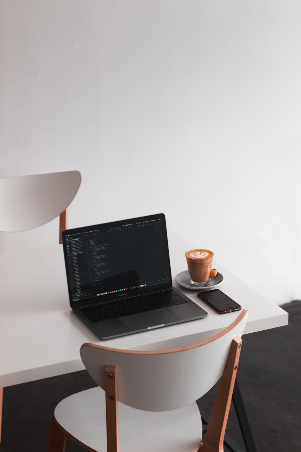 Laptop with code, latte, and phone on a white table.